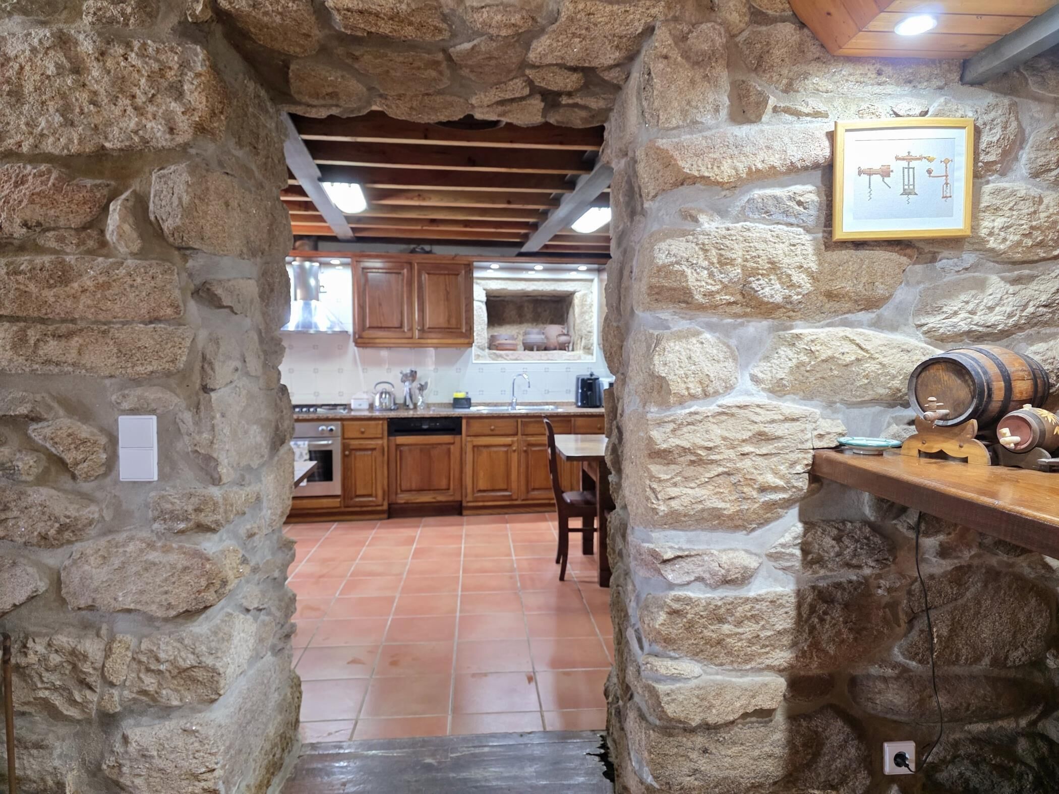 Una cocina rústica con paredes de piedra, armarios de madera, piso de baldosas y una mesa de comedor de madera.