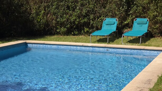 A rectangular swimming pool with clear blue water, surrounded by a concrete edge. There are two green lounge chairs positioned at the far end of the pool. - Villa Vetusta | Rustic | Pool | Northern Portugal (PENSO)