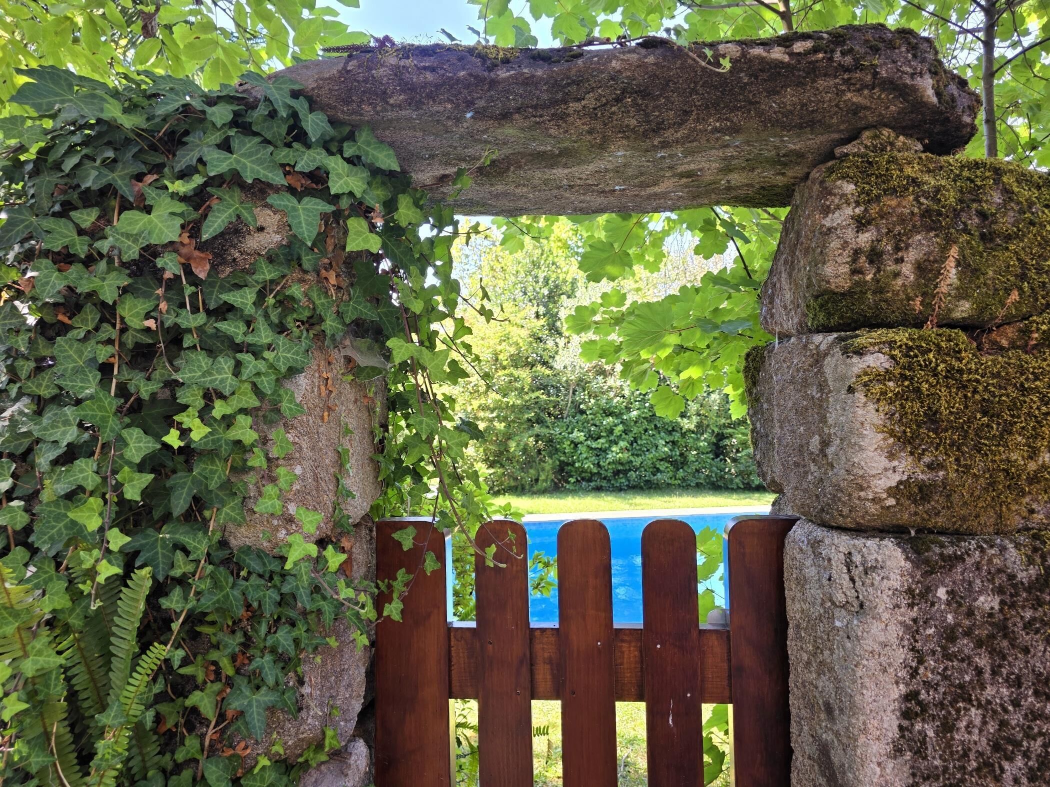 A wooden gate with a blue sign, surrounded by greenery and a stone structure.