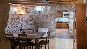 A stone-walled dining area with a wooden table and chairs, a lamp, and a view into a kitchen with wooden cabinets. - Villa Vetusta | Rustic | Pool | Northern Portugal (PENSO)