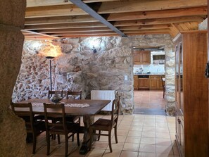 Ein Essbereich mit Stehwänden, einem Holztisch und -stühlen, einer Lampe und Blick in eine Küche mit Holzausstattung.