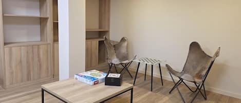 Una habitación con piso de madera, una mesa con una caja, dos sillas y un estante.