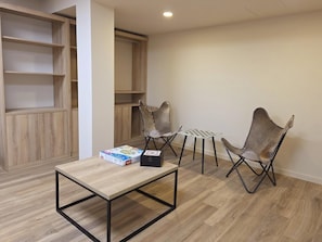 Una habitación con piso de madera, una mesa con una caja, dos sillas y un estante.