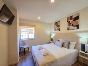 A hotel room with a bed, a chair, a desk, and a TV mounted on the wall.
