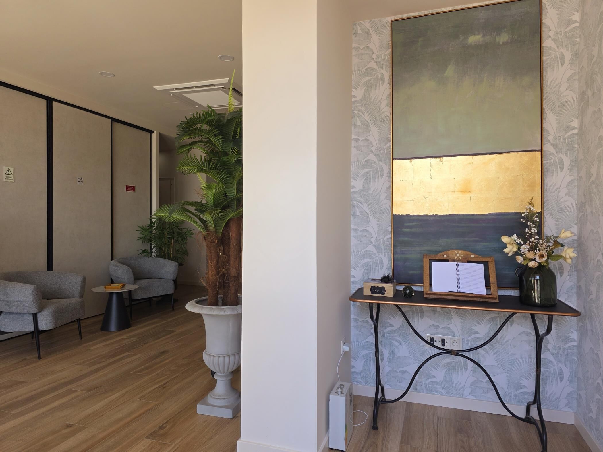 Een modern interieur met een zithoek, een grote kamerplant, een bureau met een computer en een muur met een structuur.
