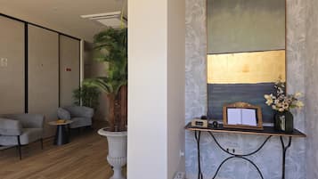 Een modern interieur met een zithoek, een grote kamerplant, een bureau met een computer en een muur met een structuur.