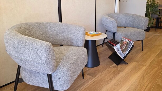 Un interior moderno con dos sillones grises, una mesita redonda y un atril para revistas.