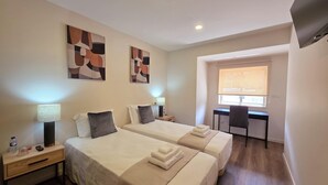 Habitación de hotel con dos camas, un escritorio, un televisor y arte abstracto en la pared.