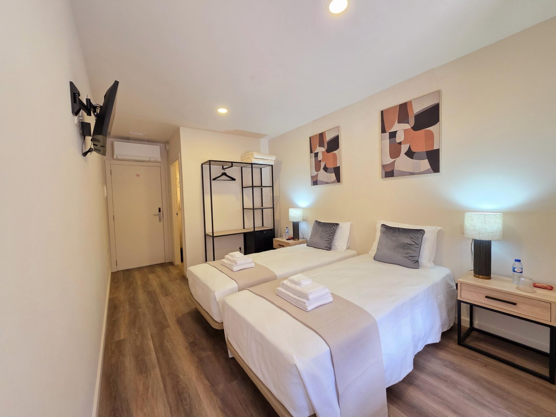 Habitación de hotel con dos camas, un armario, un escritorio con lámpara y decoración abstracta en la pared.
