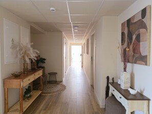 A hallway with a wooden floor, a console table with decorative items, a rug, and a painting on the wall.