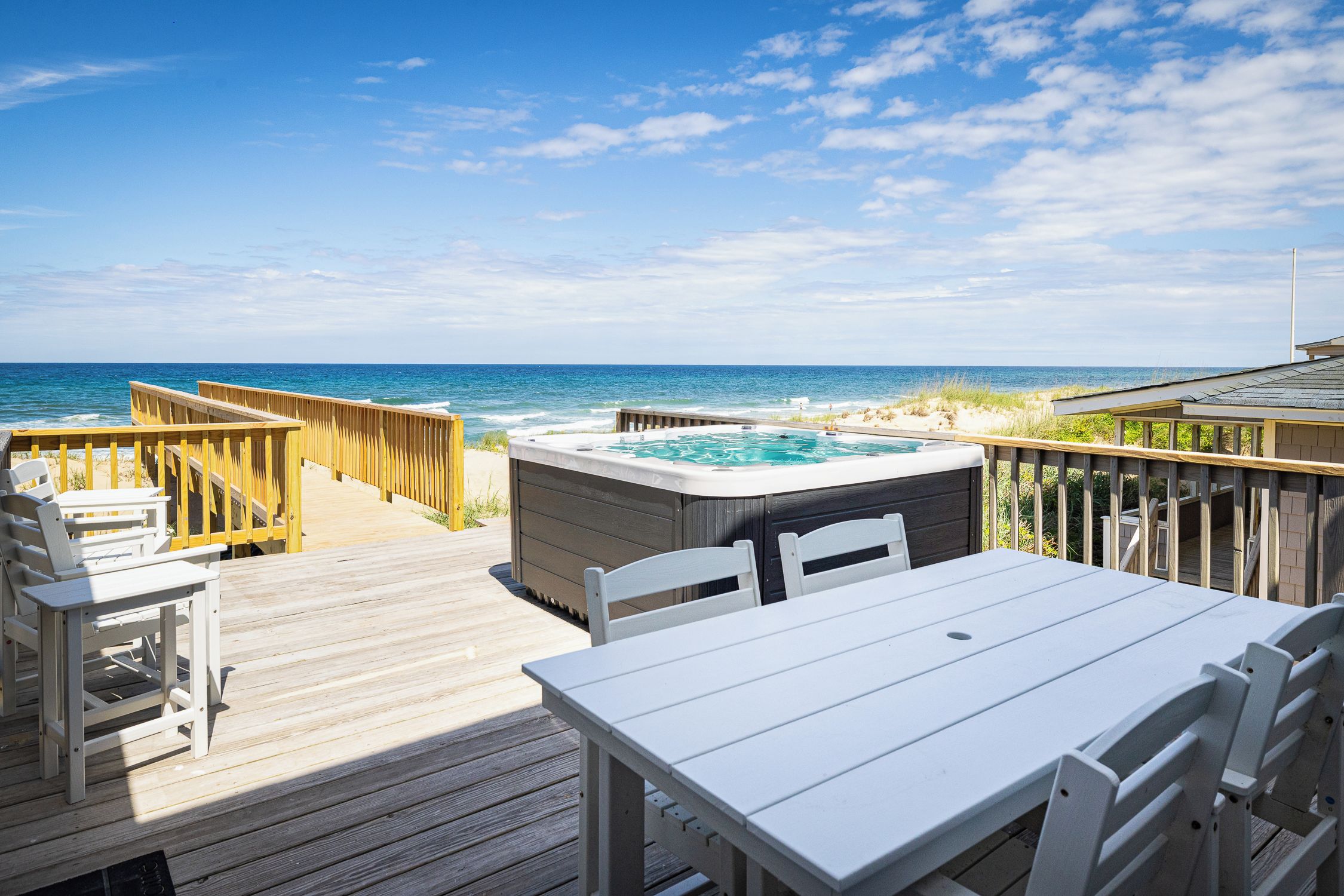 A wooden deck with a hot tub and seating area overlooking the ocean.