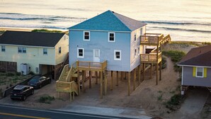 A beachfront house with a wooden deck and a staircase leading to a second floor. - Spacious 5-bedroom house in charming Kitty Hawk with AC (Kitty Hawk)