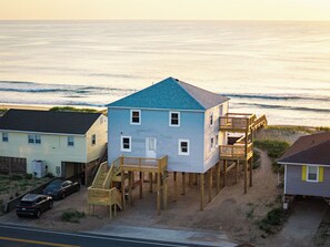Ein Strandhaus mit einer Holzterrasse und einer Treppe, die zu einem zweiten Stock führt.