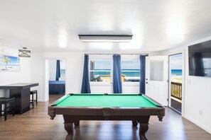 Ein Billardtisch in einem Raum mit Blick auf das Meer durch große Fenster.