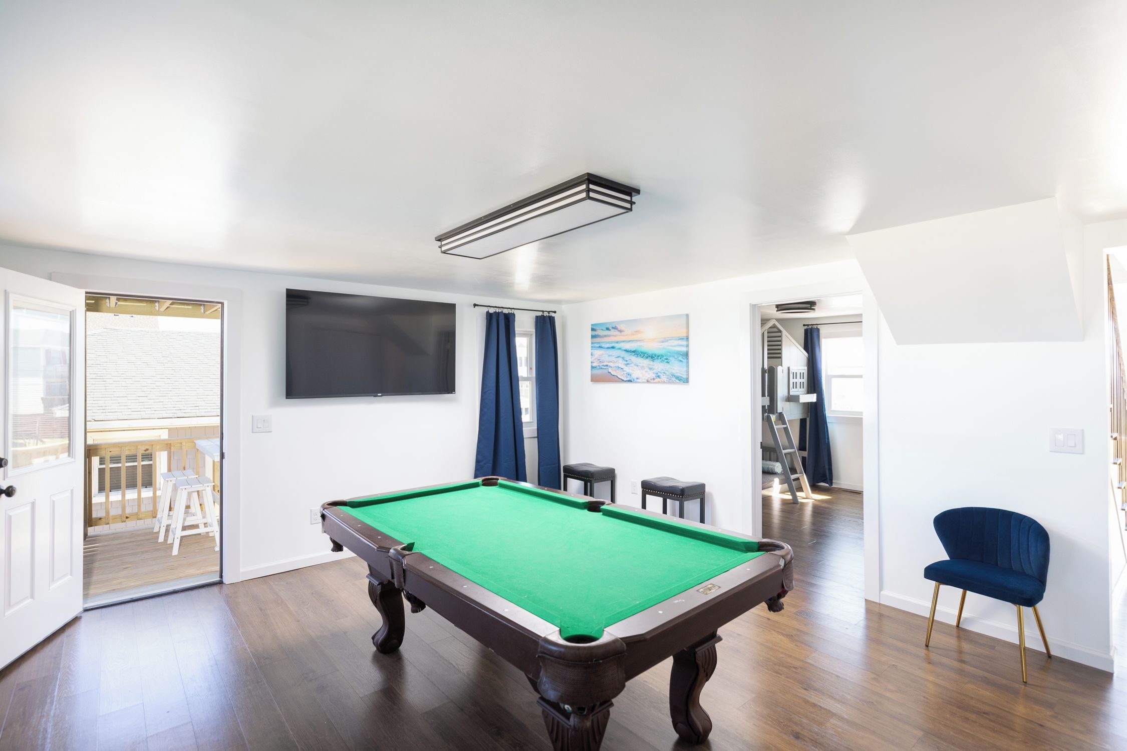 A pool table in a room with a wooden floor, a television mounted on the wall, and a painting above it.