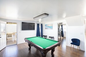 Een biljart in een kamer met een houten vloer, een aan de muur bevestigde televisie en een schilderij erboven.