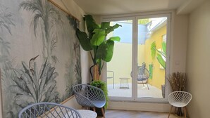 Habitación con un gran ventanal corredero que da a un espacio exterior, con dos sillas y una planta en maceta.