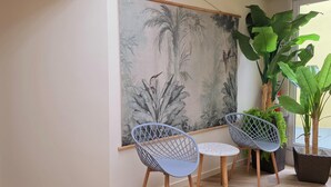 Una habitación con un gran mural en la pared, dos sillas, una planta en maceta y una ventana.