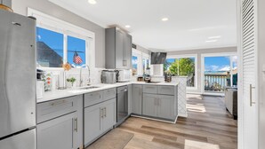 Cozinha moderna com armários cinzas, eletrodomésticos de aço inoxidável e uma grande janela com vista para um terraço.