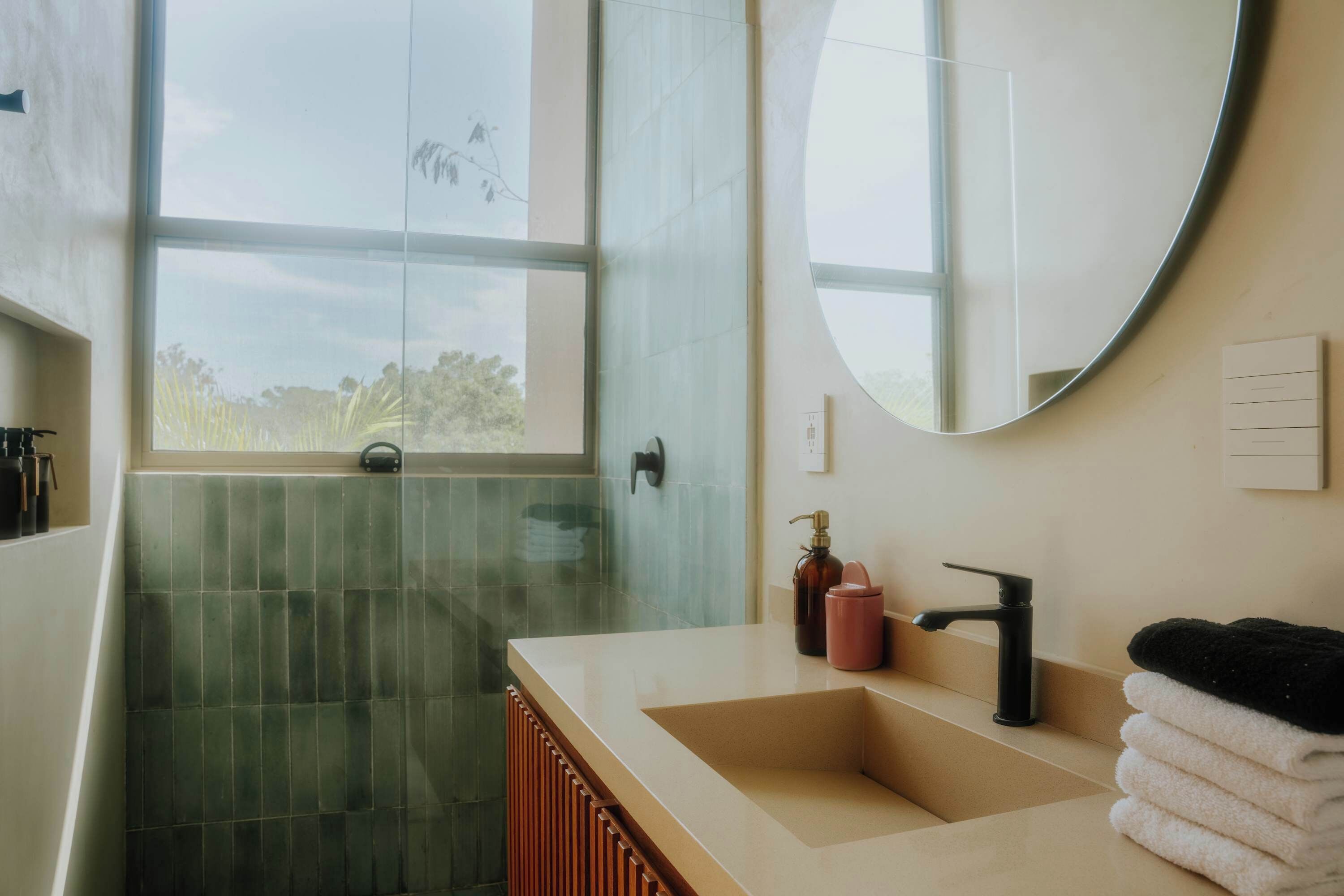 Une salle de bain avec une grande fenêtre, un lavabo, un miroir et une douche.
