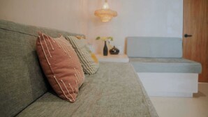 Un salon moderne avec un canapé vert, un coussin marron, une petite table sur laquelle est posé un vase, et un luminaire suspendu.
