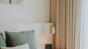 Une chambre d’hôtel avec un lit, des oreillers, une table de chevet, une lampe et une fenêtre avec des rideaux.