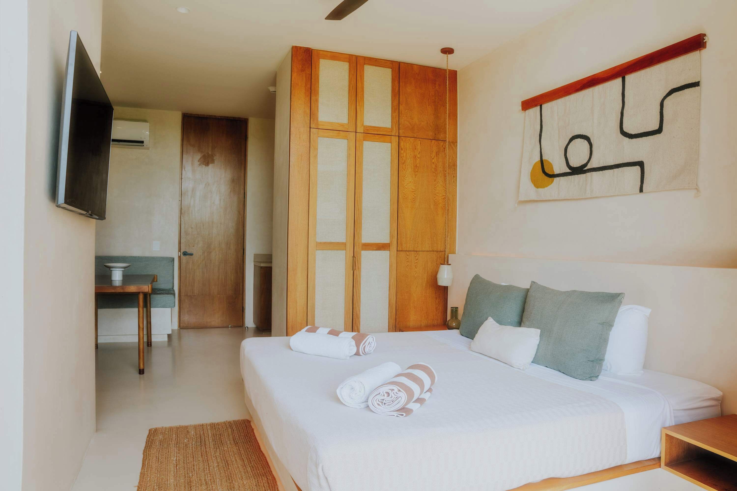 A hotel room with a bed, a TV, a wooden wardrobe, and a painting on the wall.