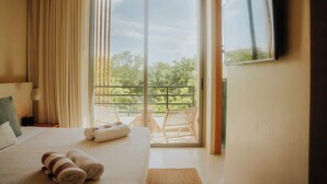 Une chambre d’hôtel avec un lit, une télévision, un balcon avec des chaises et une vue sur la verdure.