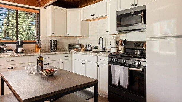 Una cocina con armarios blancos, estufa, microondas y refrigerador.