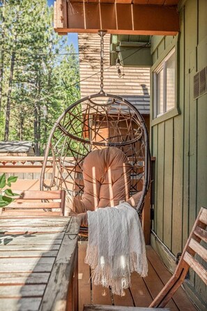 Une terrasse en bois avec un fauteuil suspendu, une couverture blanche à franges et un banc en bois.