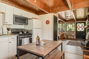 A kitchen with a microwave, stove, and refrigerator. There is a dining table with a bottle of wine and glasses. - Solheim Lodge| Hot Tub, Fire Pit, EV Charger, Pets (Big Bear Lake)