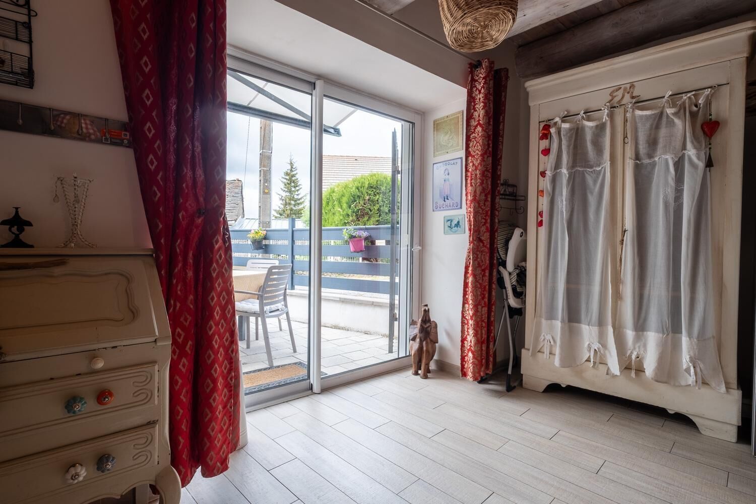 Een kamer met een schuifdeur naar een balkon, een dressoir met laden, een stoel en een klein beeldje.