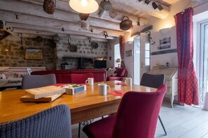 A cozy dining area with a wooden table, red upholstered chairs, and a stone wall with kitchenware. - Oya Vacation Rental - CHAUDEYRAC - Vacation Rental (CHAUDEYRAC)