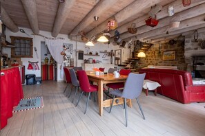 A rustic interior with a wooden dining table, red and grey chairs, a red sofa, and various kitchen utensils hanging on the walls. - Oya Vacation Rental - CHAUDEYRAC - Vacation Rental (CHAUDEYRAC)