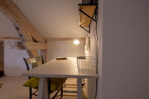A dining area with a white table, green chairs, a metal basket, and a pendant light. - Oya Vacation Rental - CHAUDEYRAC - Vacation Rental (CHAUDEYRAC)