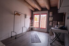 A room with a wooden ceiling, a chair, a table with an ironing board, and a window with red curtains. - Oya Vacation Rental - CHAUDEYRAC - Vacation Rental (CHAUDEYRAC)