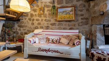 Um quarto acolhedor com parede de pedra, escada de madeira, sofá branco com a palavra 'Bienvenue' escrita e um candeeiro pendente, além de uma pintura de um campo.