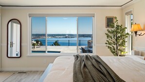 Une chambre avec une grande fenêtre, un lit, un miroir, une plante et une lampe.