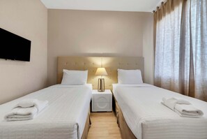 A hotel room with two beds, a flat-screen TV mounted on the wall, a bedside lamp, and a window with curtains. - Modern Townhome with Grill and Balconies (Kissimmee)