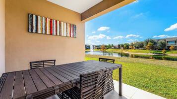 A patio with a table and chairs, a colorful abstract painting on the wall, and a view of a building complex and water feature.