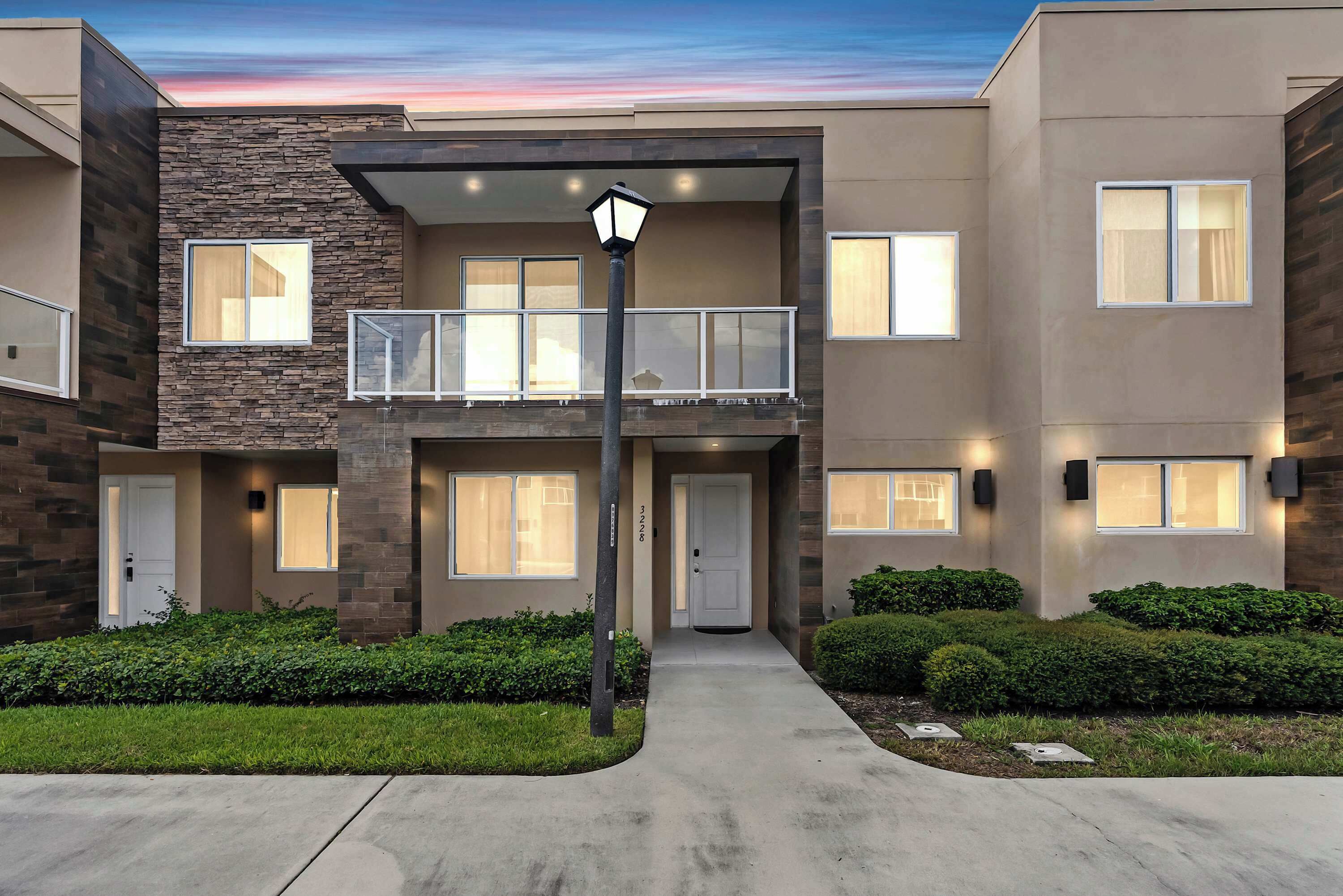 A modern multi-story residential building with a balcony, a front door, and a well-maintained lawn.