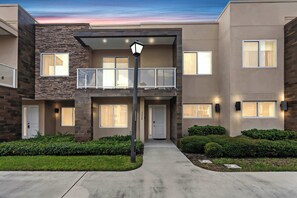A modern multi-story residential building with a balcony, a front door, and a well-maintained lawn. - Modern Townhome with Grill and Balconies (Kissimmee)