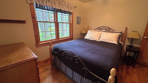 Um quarto com cama, janela, mesa de cabeceira, luminária e cômoda.