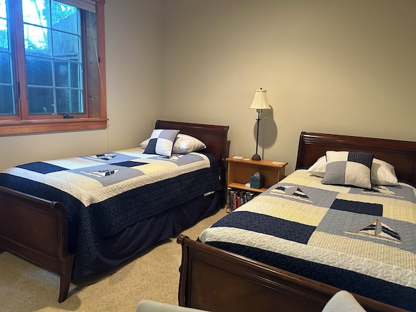 Two single beds with wooden headboards, a bedside table with a lamp, and a window with a view of trees.