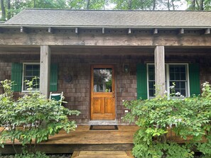 A wooden house with a front door, green shutters, and a porch.