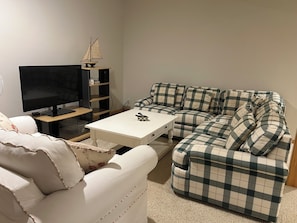 A living room with a television, a small table, a sofa, and a decorative sailboat model.