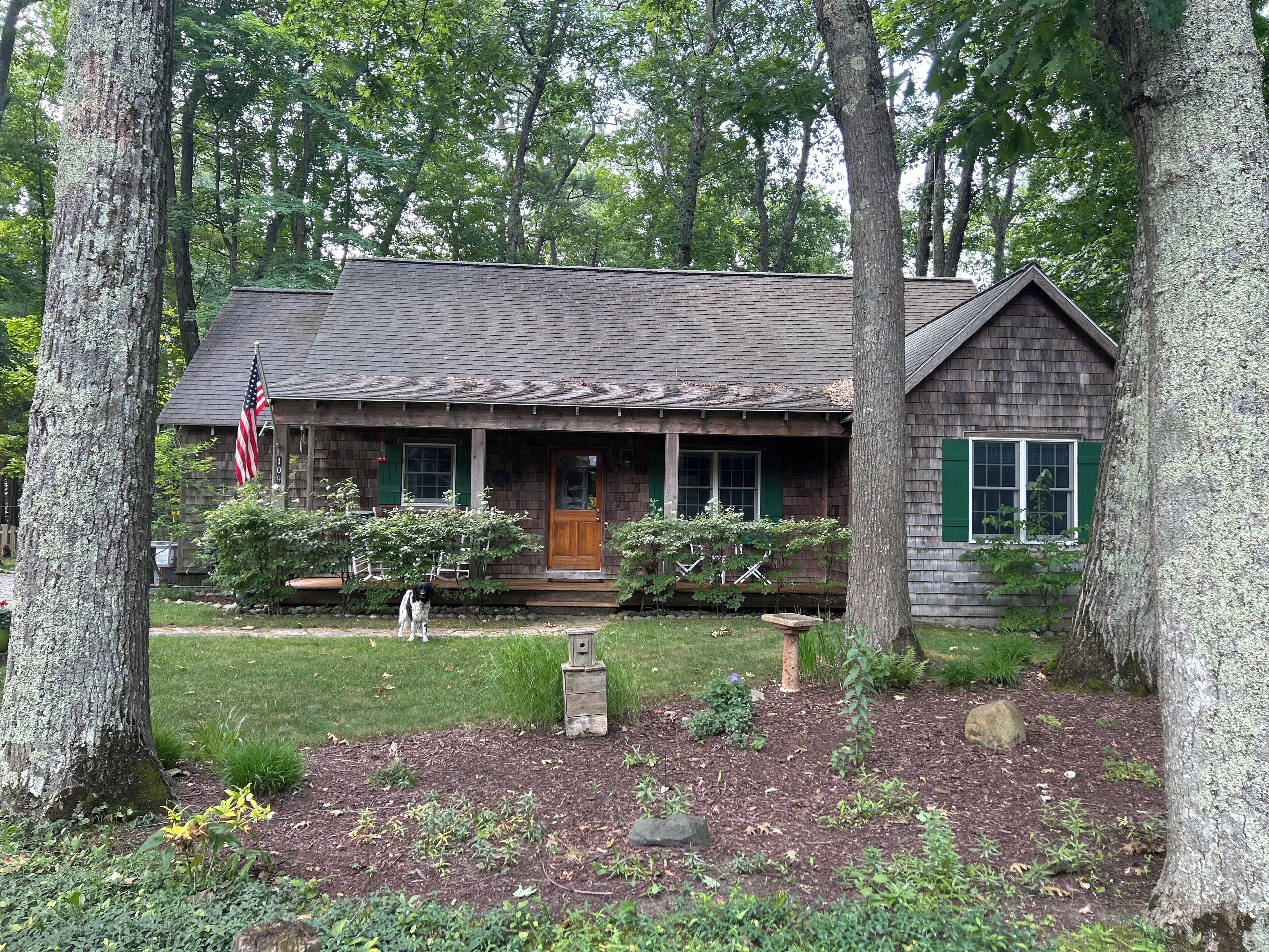 A rustic cabin with a front porch, a small garden, and a flag.