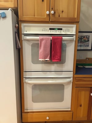 A kitchen with a double oven, wooden cabinets, and a clock displaying 11:46.