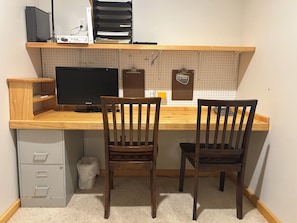 A study area with a desk, two chairs, a computer monitor, and a pegboard wall.