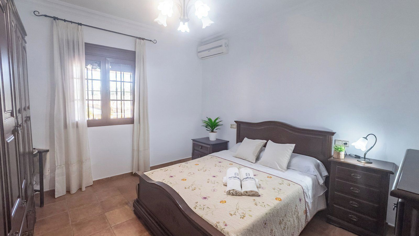 A bedroom with a bed, a nightstand, a dresser, a window with curtains, and an air conditioning unit.